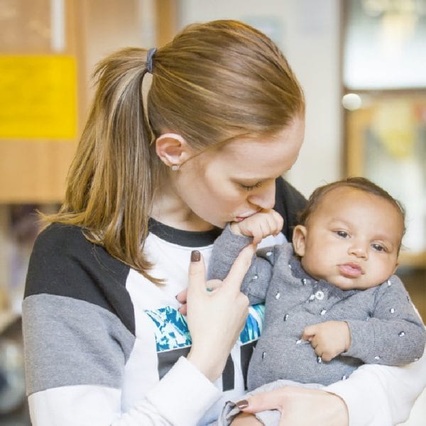 Woman holding a baby and kissing its hand.